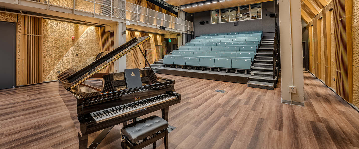 Concert hall with a grand piano in the center and seating in the background.
